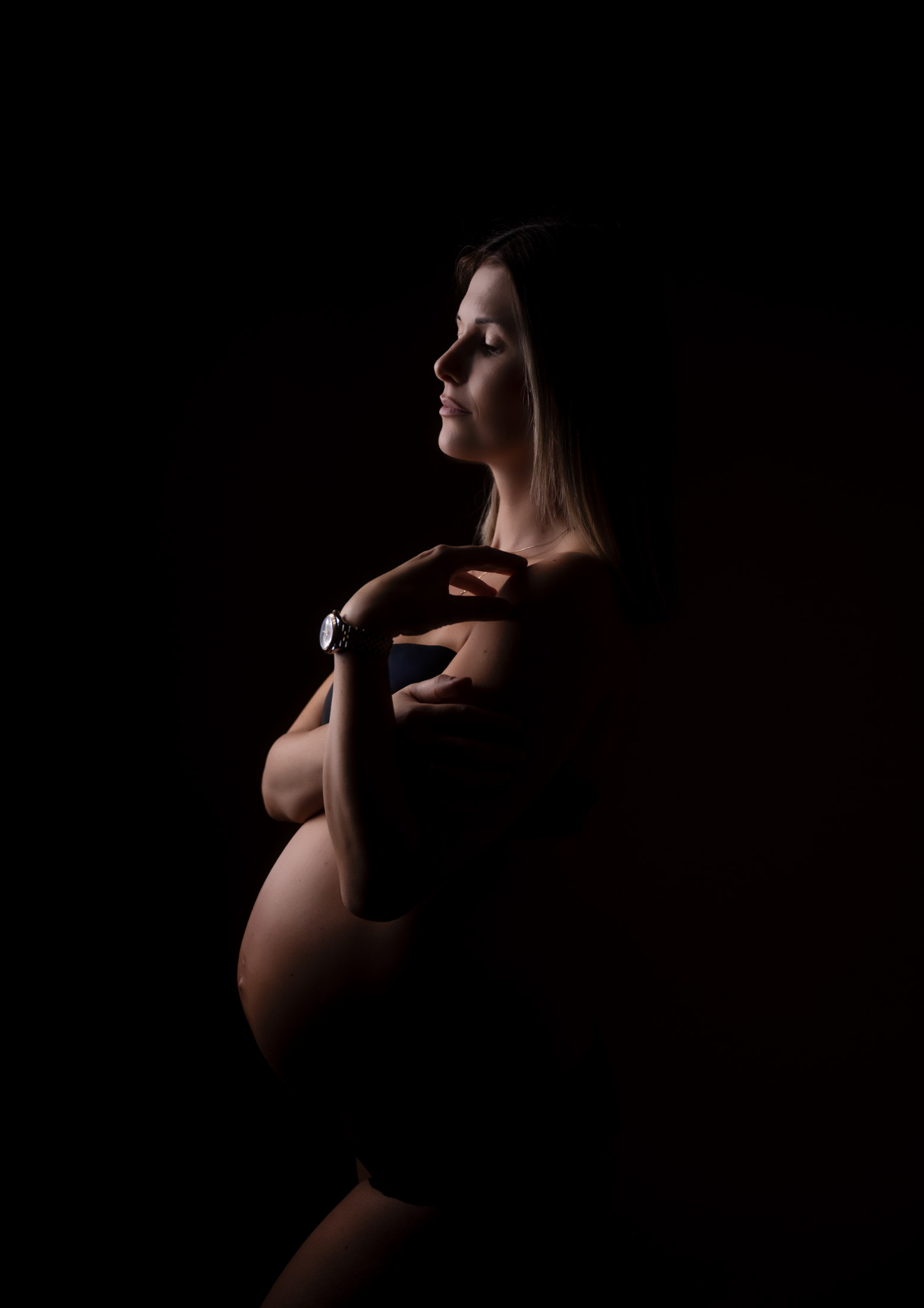 Schwangere im Profil vor schwarzem Hintergrund, Studiofotografie mit Lichtakzent