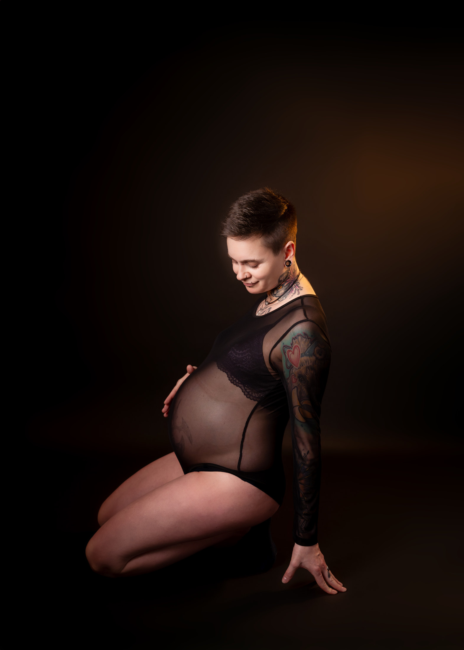 Schwangere kniend im transparenten Bodysuit im Fotostudio