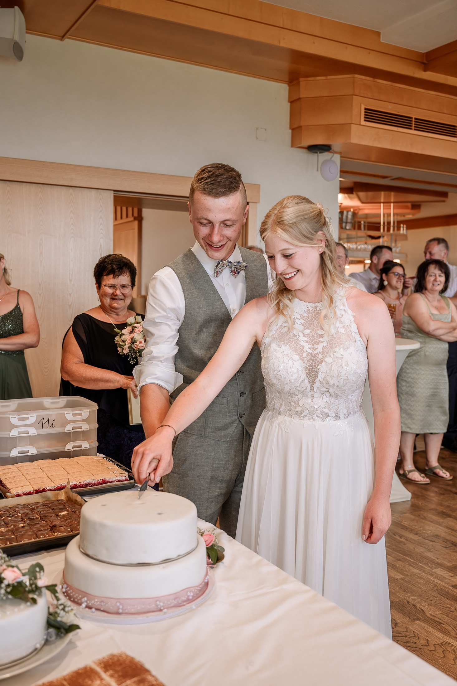 Brautpaar mit Hochzeitstorte, Gäste schauen zu