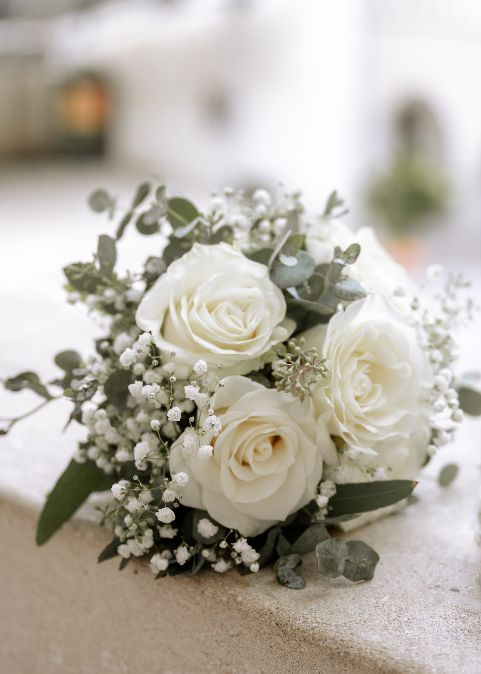 Brautstrauß mit weißen Rosen und Schleierkraut auf einer Steinbrüstung