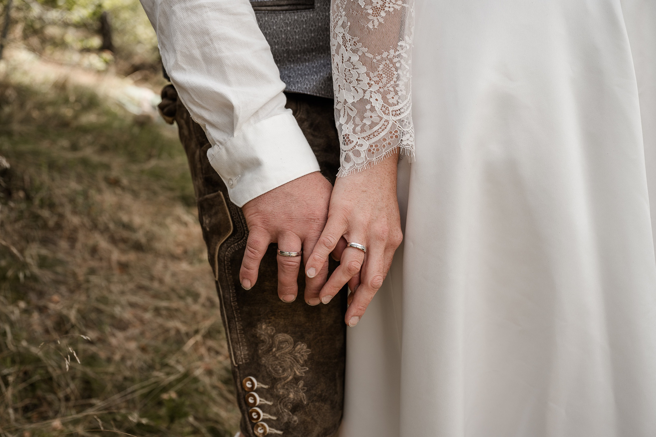 Hände von Braut und Bräutigam in Tracht mit Eheringen