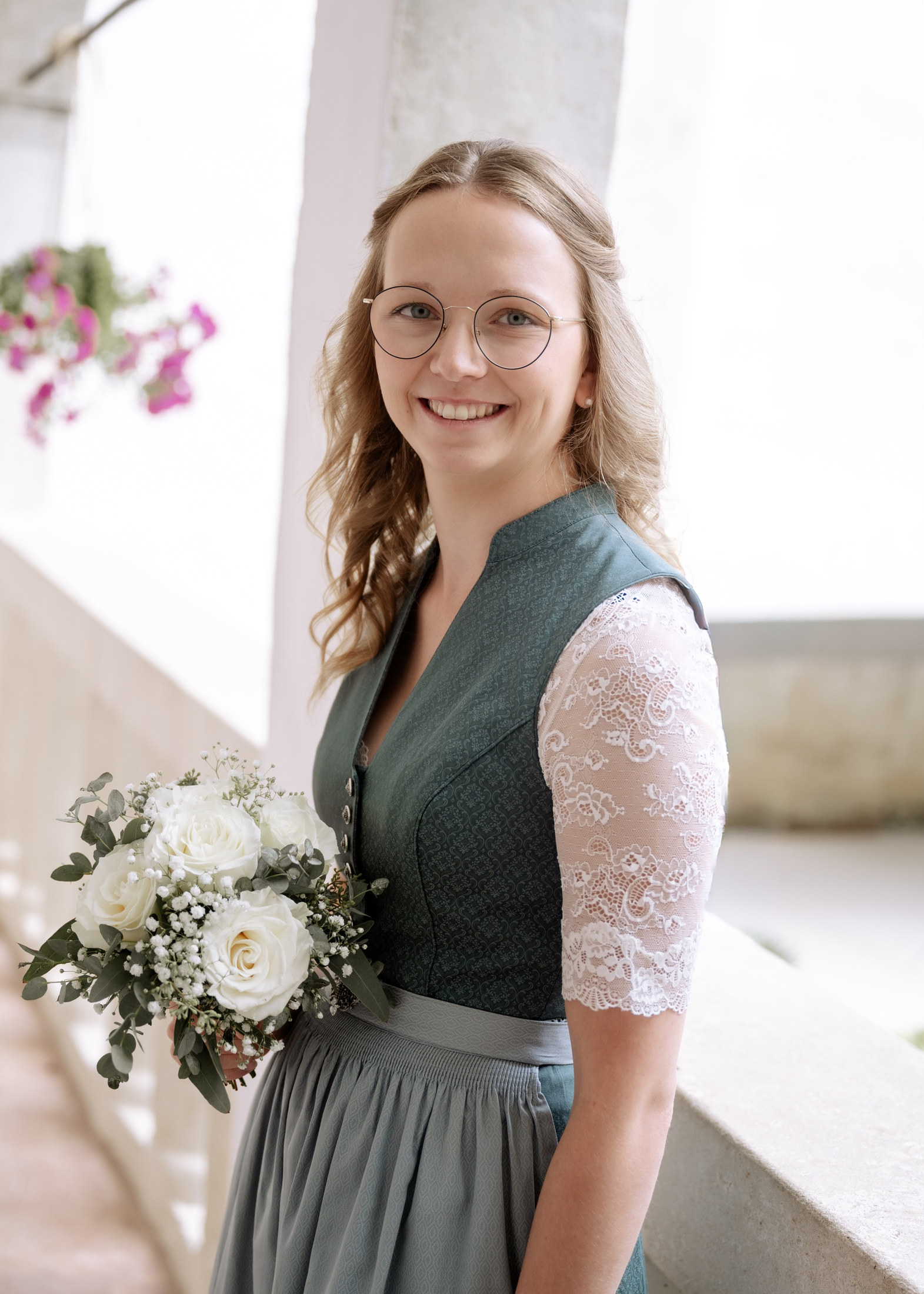 Lächelnde Braut im Dirndl mit weißem Brautstrauß im Schlossgang