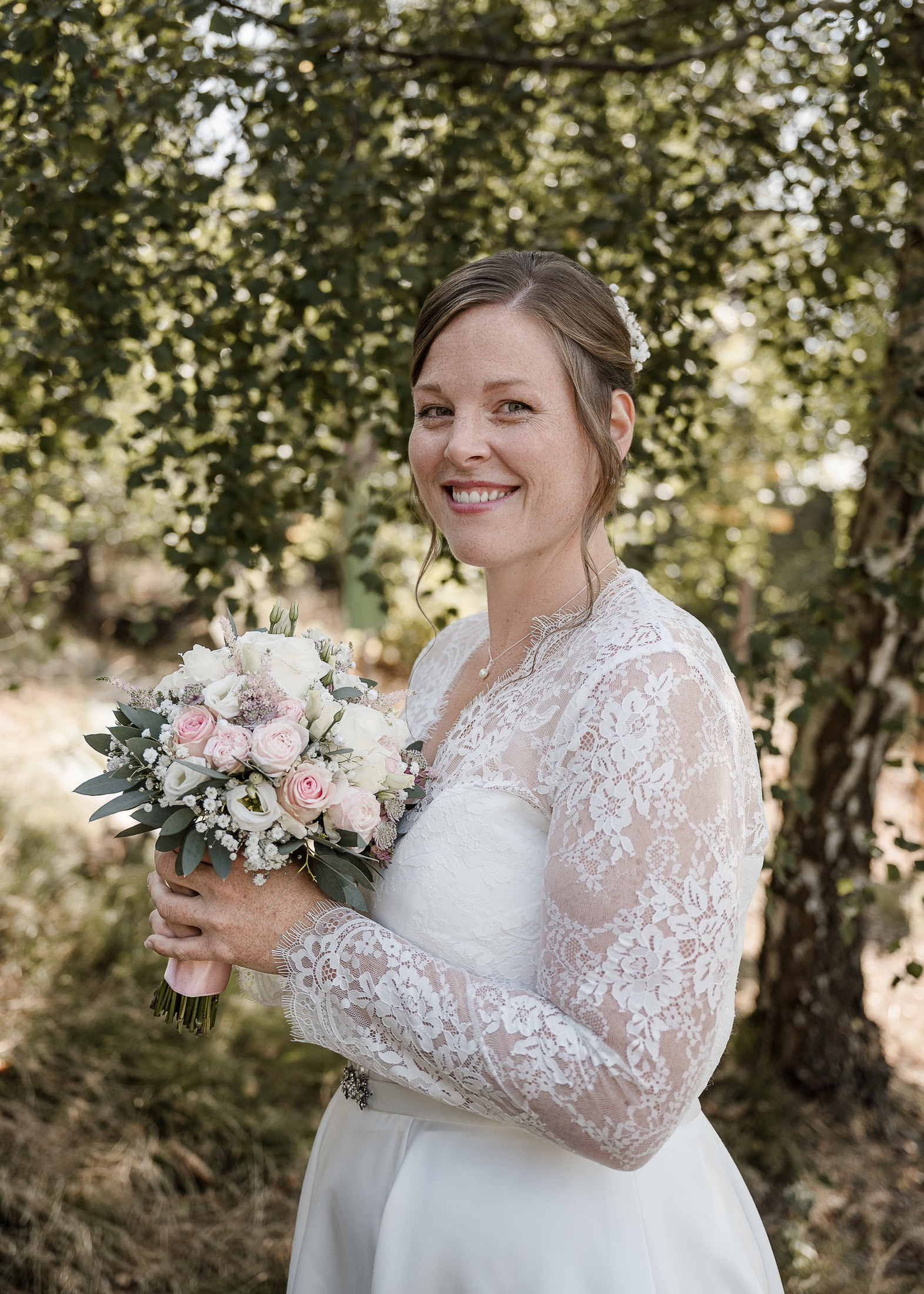 Lächelnde Braut mit rosa Brautstrauß vor Birken