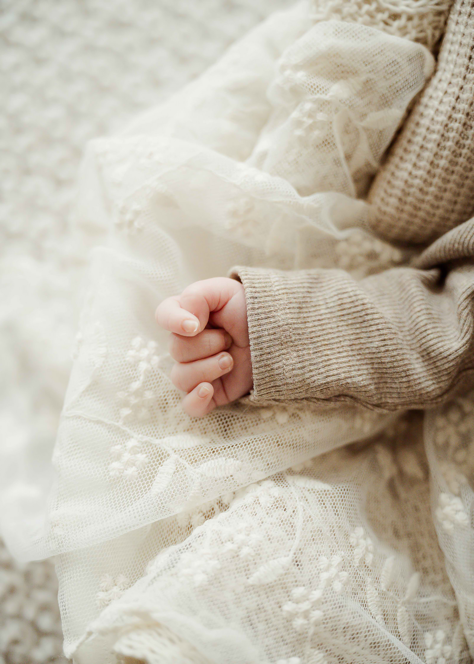 Nahaufnahme einer winzigen Babyhand zwischen Spitzenstoff