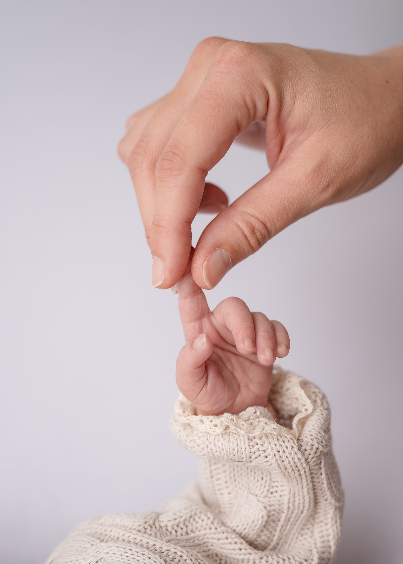 Babyhand und Finger der Mutter, Strickärmel