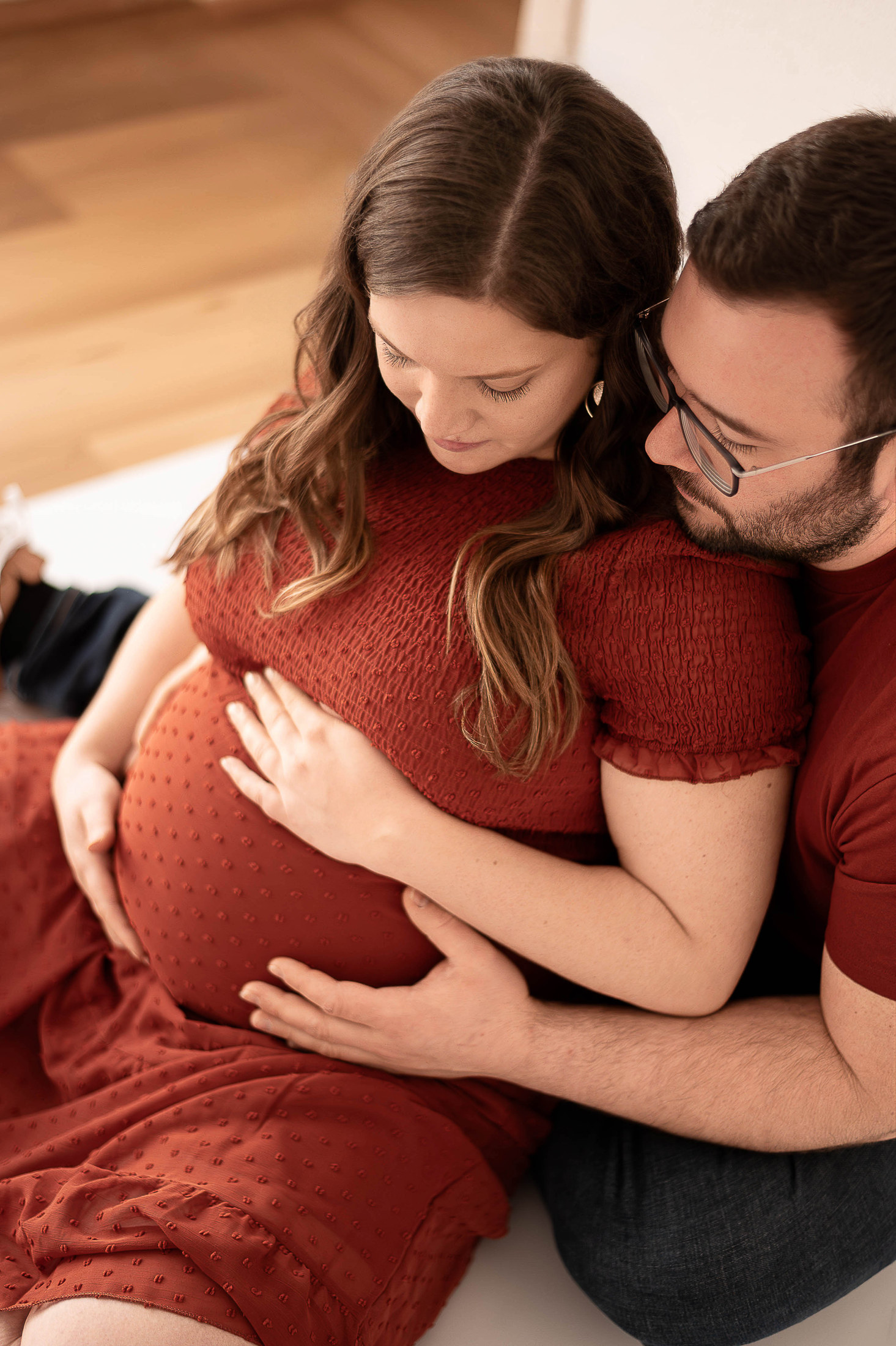 Paar sitzt gemeinsam am Boden und umarmt den Babybauch