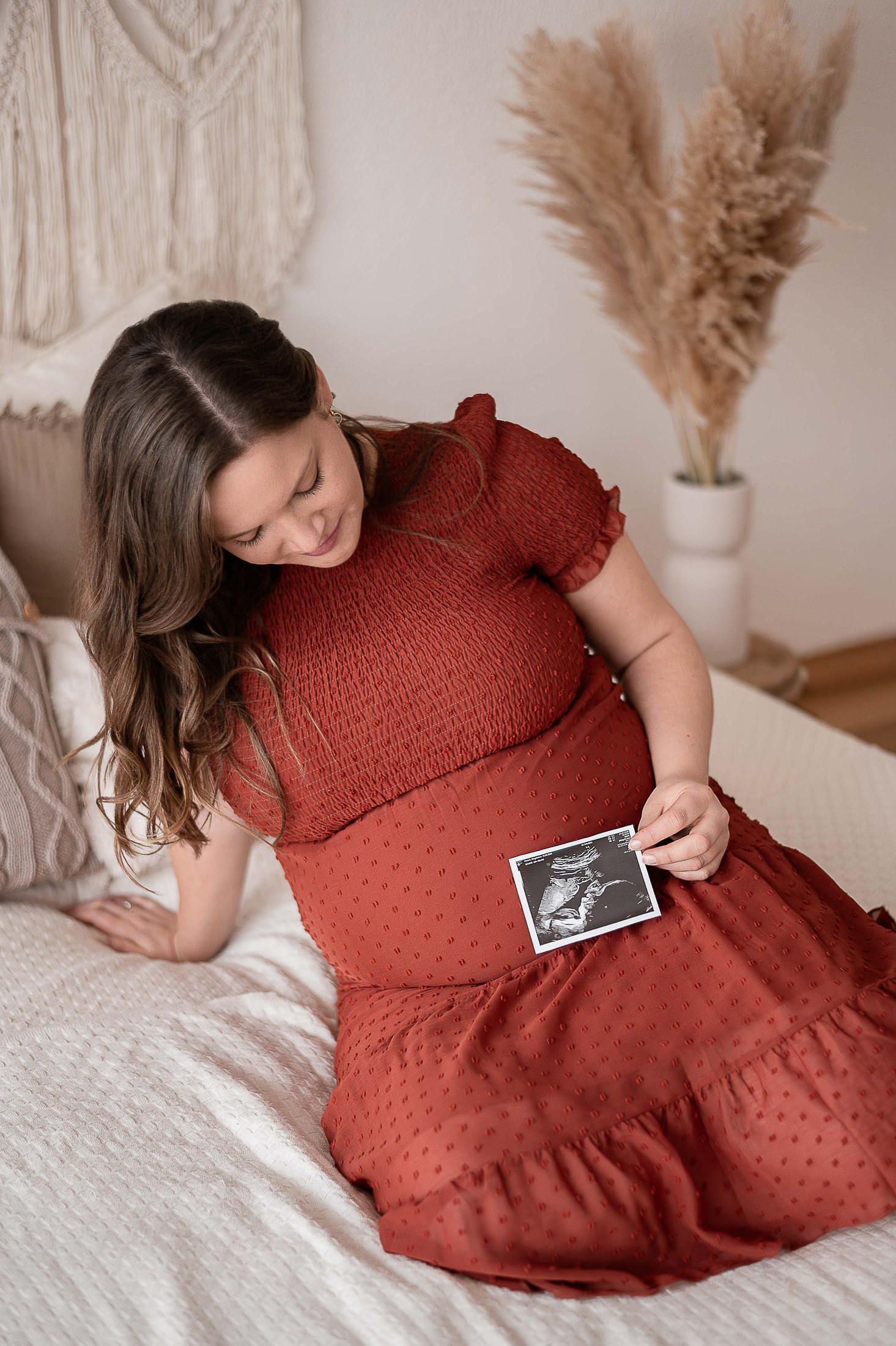 Schwangere Frau betrachtet Ultraschallbild ihres Babys im Bett