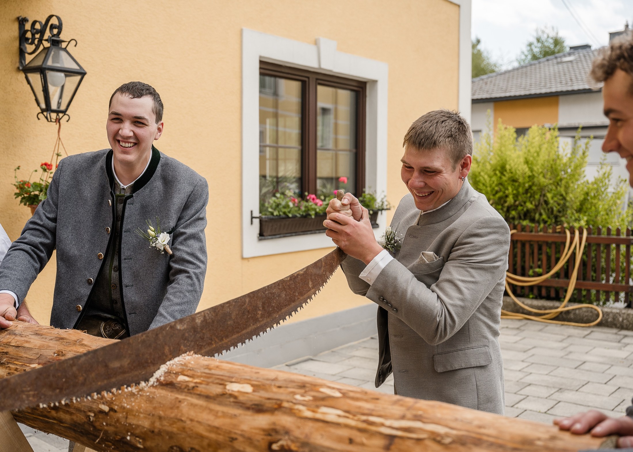Bräutigam und Trauzeuge lachen beim Baumstammsägen